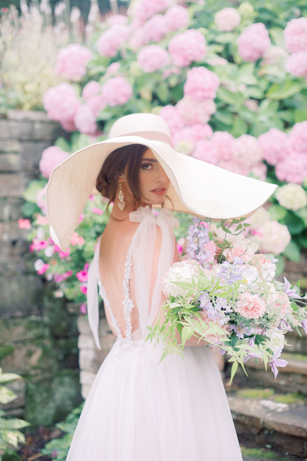 Bride in sunhat holding bouquet of flowers at Hedsor House, England