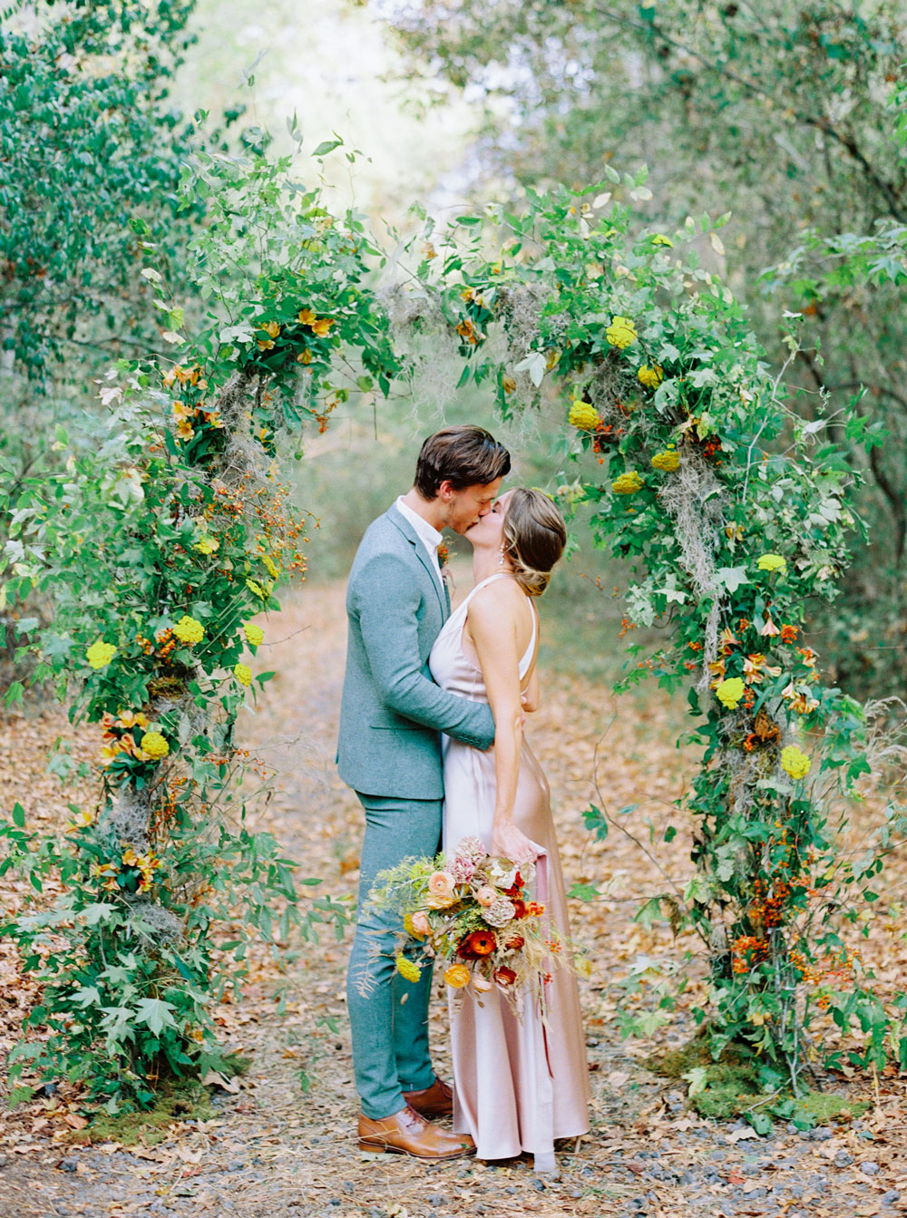 Couple kiss underneath a foliage and wildflower arch in the woods