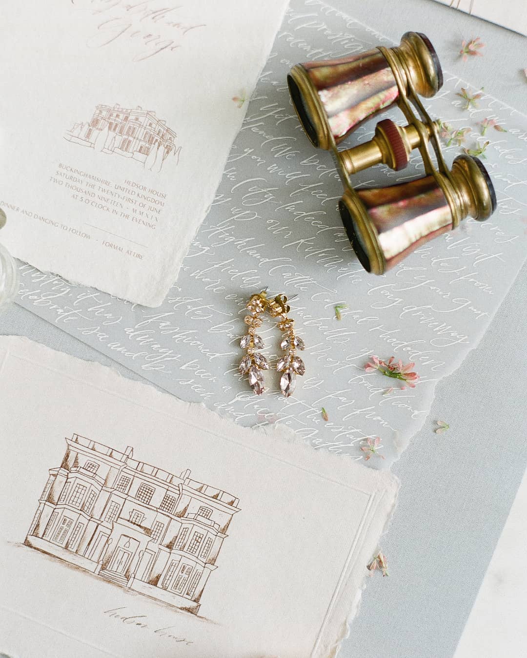 drip crystal bridal earrings atop calligraphed vellum and a custom sketch of an English manor house