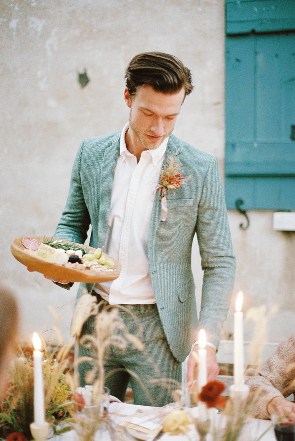 autumn wedding dinner with groom in a sage green suit passing the charcuterie board