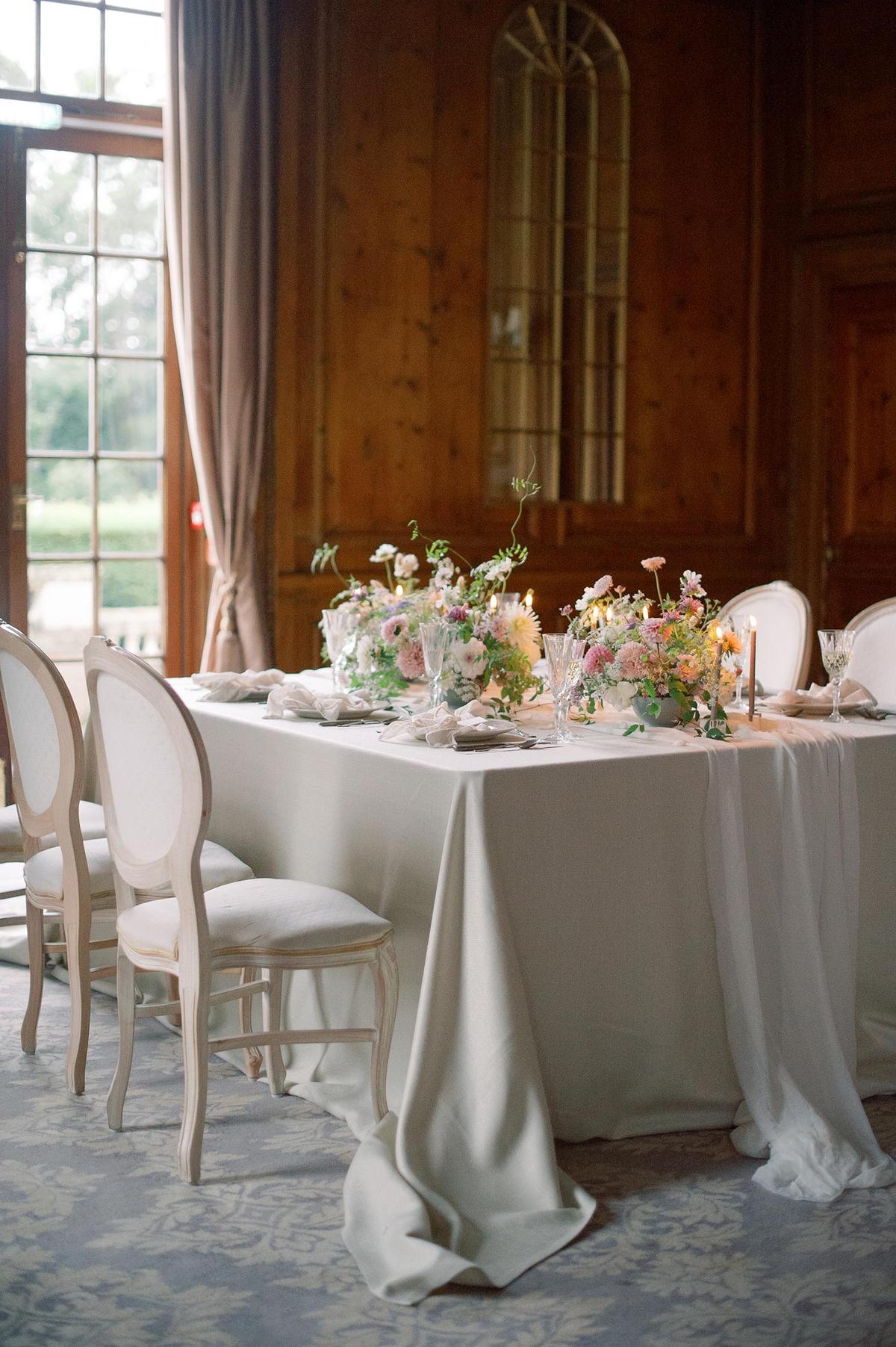 spring ballroom wedding reception with a neutral table linen, soft silk runner and low garden centerpieces mixed with skinny taper candles; photography by Julie Livingston at an English country estate Hedsor House with planning and design by Willow and Oak Events