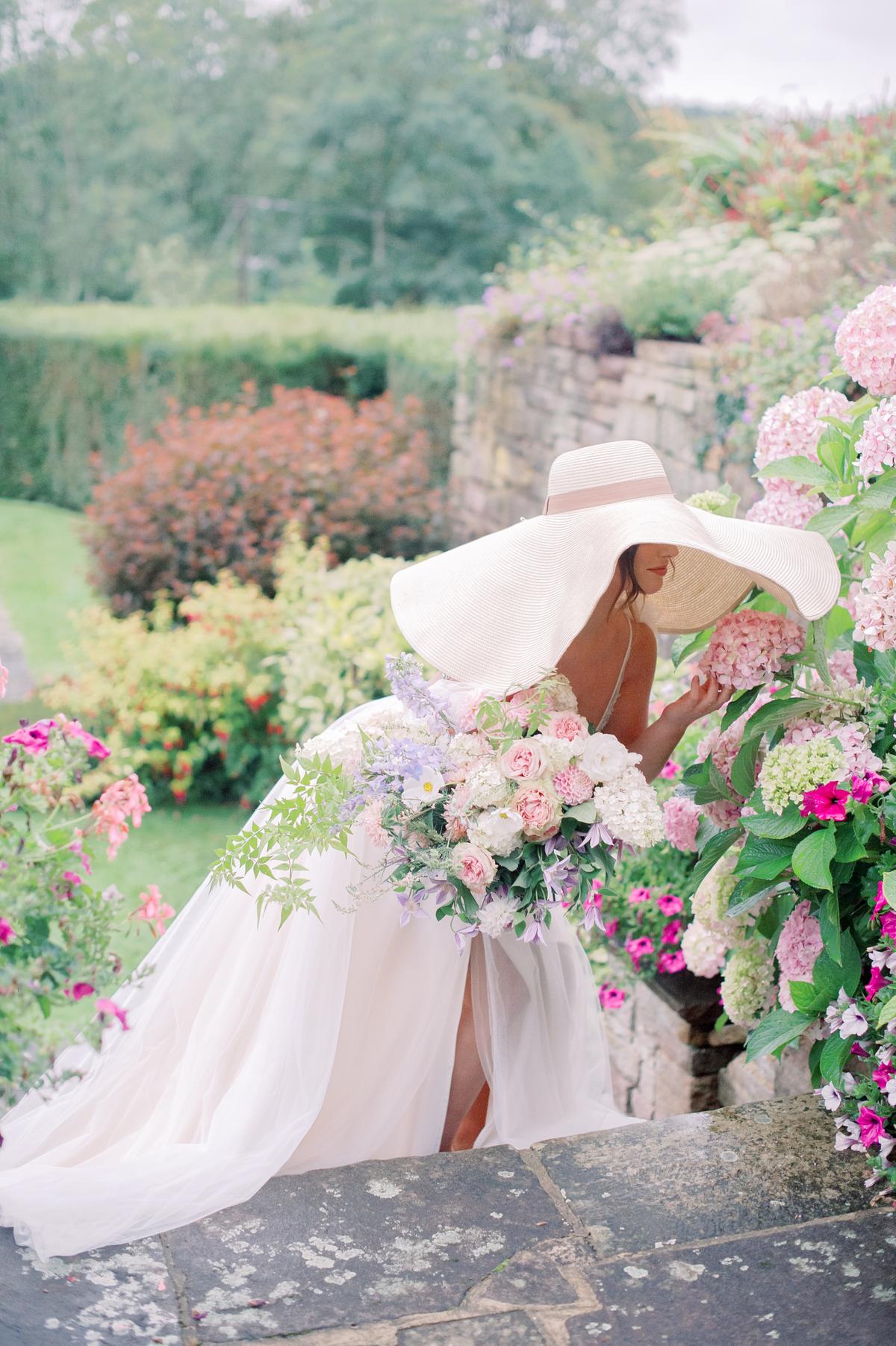English garden wedding with bride in a flowy silk gown, wild organic pastel bouquet and oversized sun hat; photography by Julie Livingston at an English country estate Hedsor House with planning and design by Willow and Oak Events