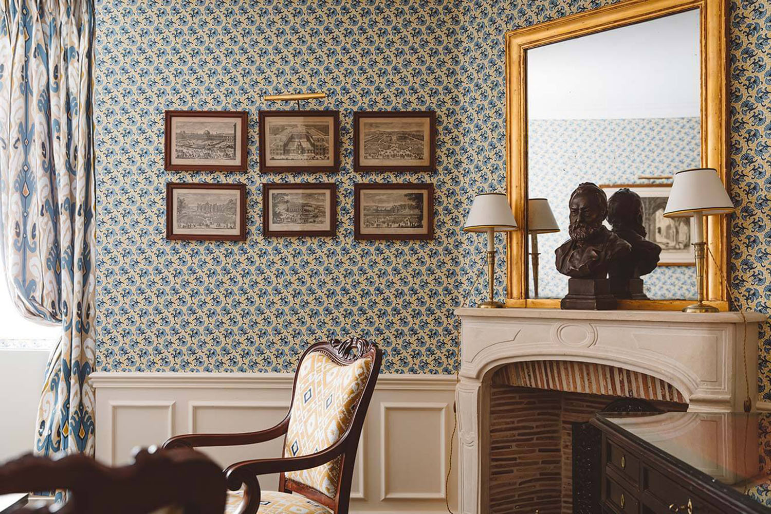 A blue floral wallpapered guest room at Hôtel de l'Abbaye with a vintage mahogany armchair and working wood fireplace