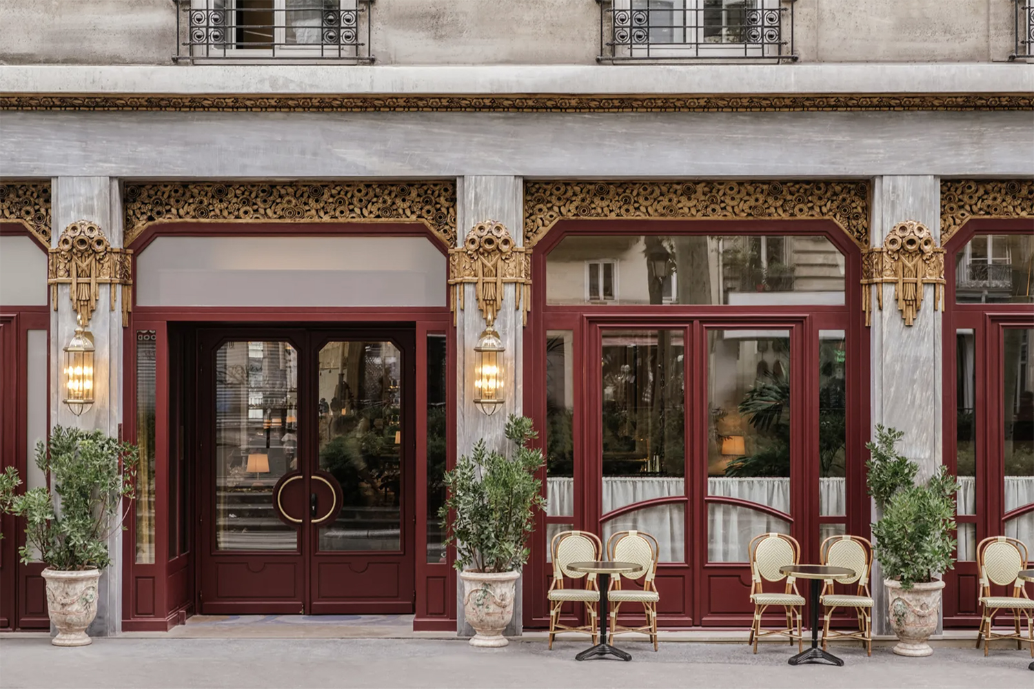A stone + red lacquered exterior in an Art Deco style for Hotel Rochechouart with small bistro tables and vintage rattan chairs with cream cane-weave