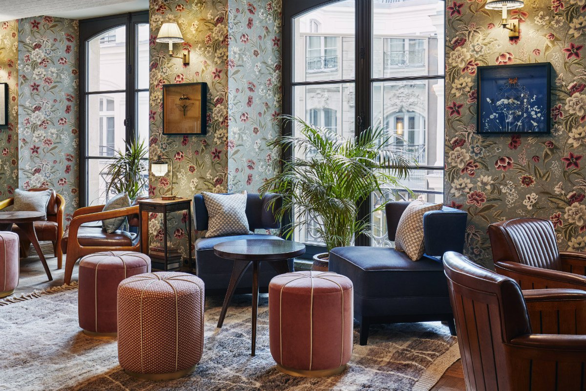 Jacque's Bar at The Hoxton Paris, with Marrakesh's Majorelle garden as the inspiration behind the design. Intricate floral wallpaper and plush lounge furniture fill the room, alongside upholstered poufs and accent cushions. 