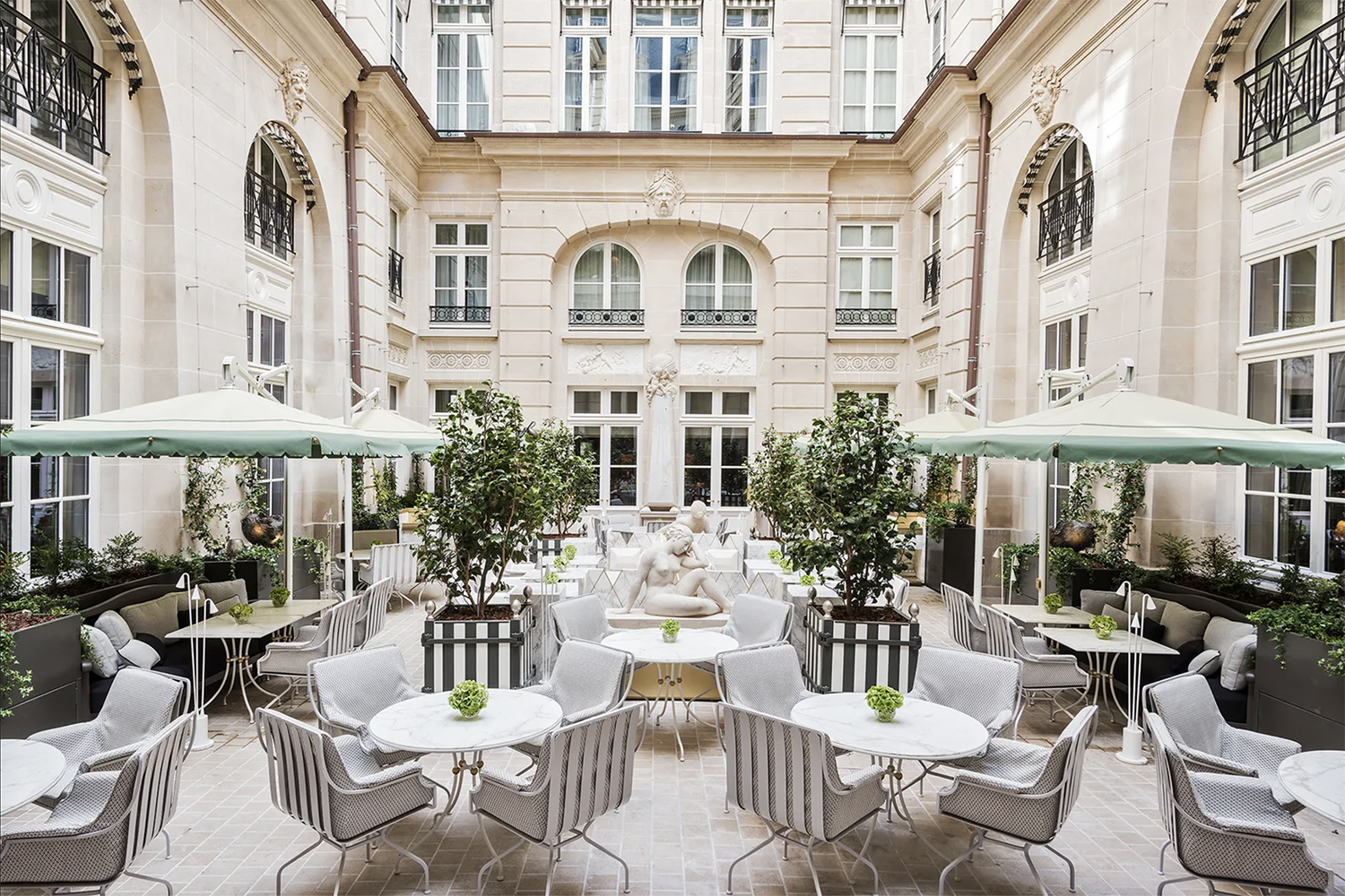 The inner courtyard restaurant of Hotel de Crillon in Paris with white and gray furniture and pastel green umbrellas