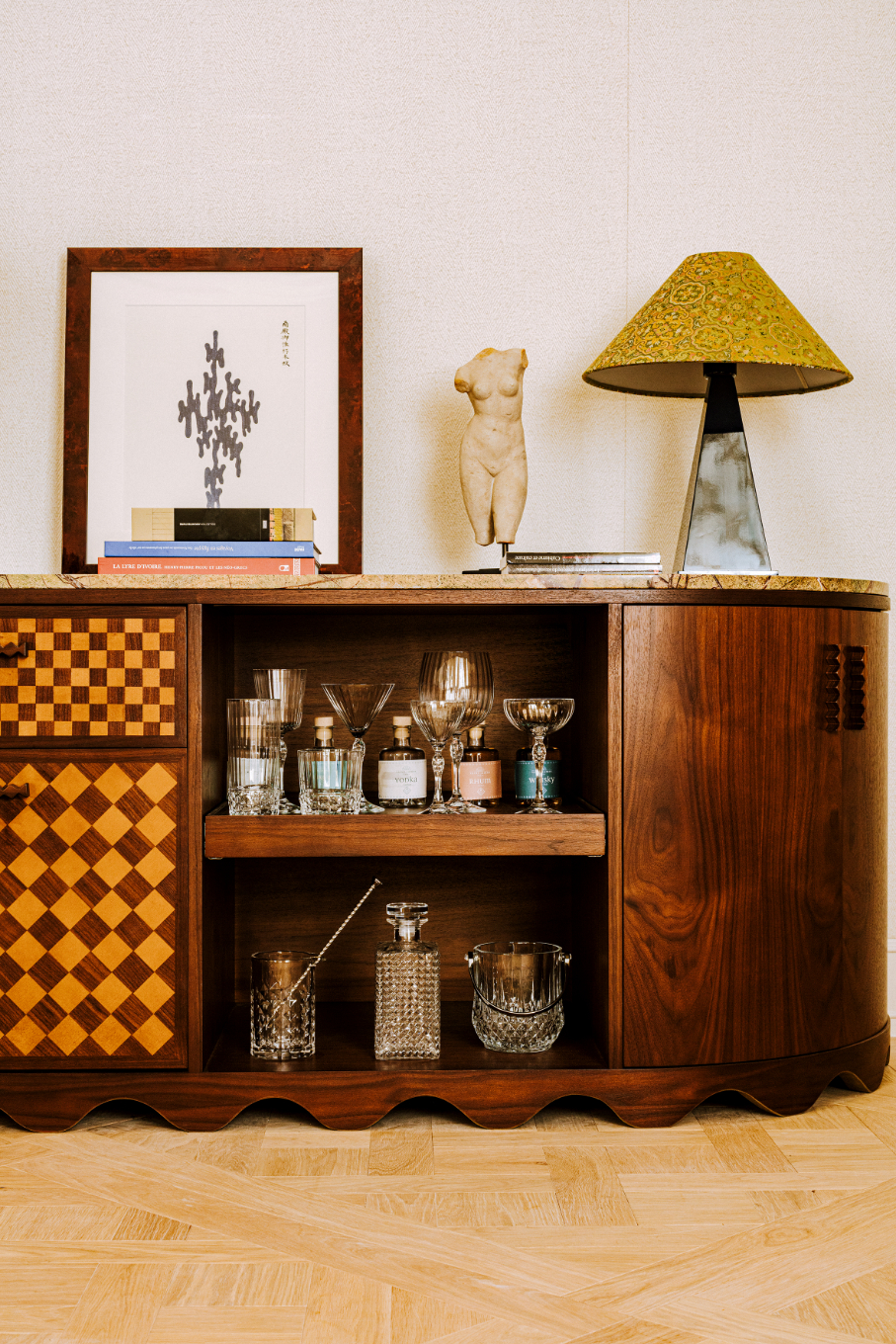 A scalloped wooden sideboard with a checkerboard facade and mini bar utensils and glassware