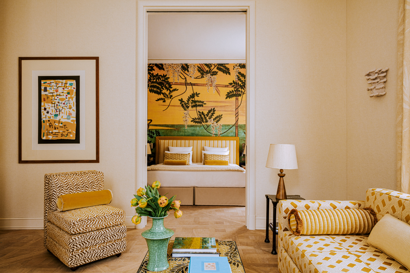 A golden-hued Junior Suite at Saint James Paris with African inspired prints, green marbled vases, wisteria printed wallpaper, contemporary art and plush sofas
