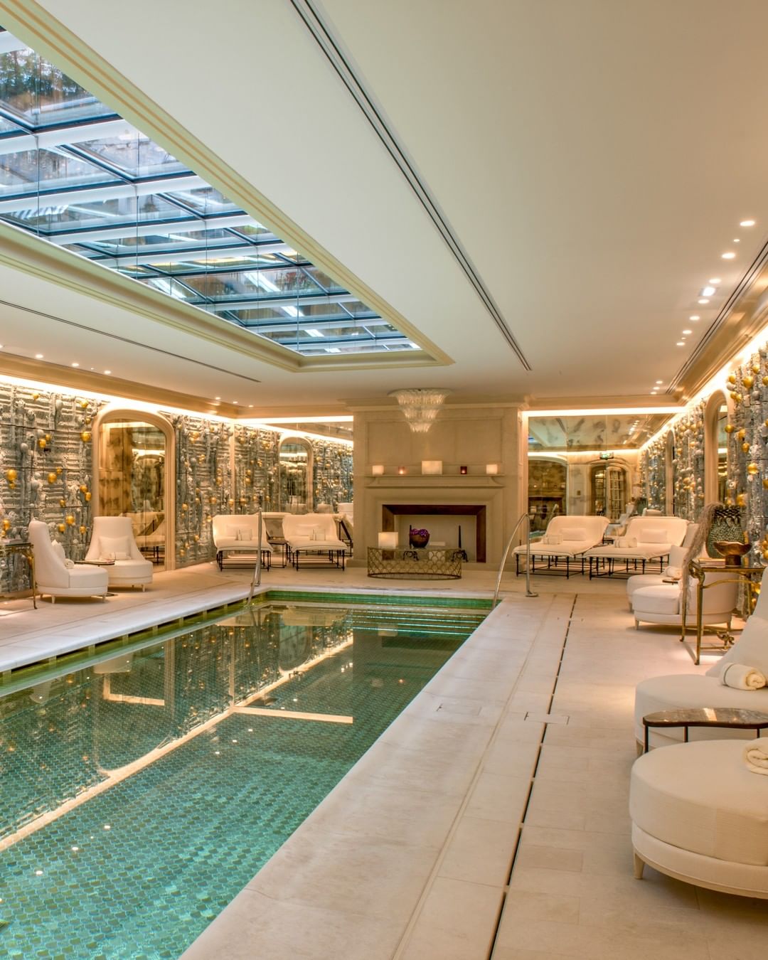 The luxe pool at Hotel de Crillon Paris with white lounge furniture, stone floors, mirrored walls and 17,600 gold scales at the base of the pool to give the water a glistening siren effect