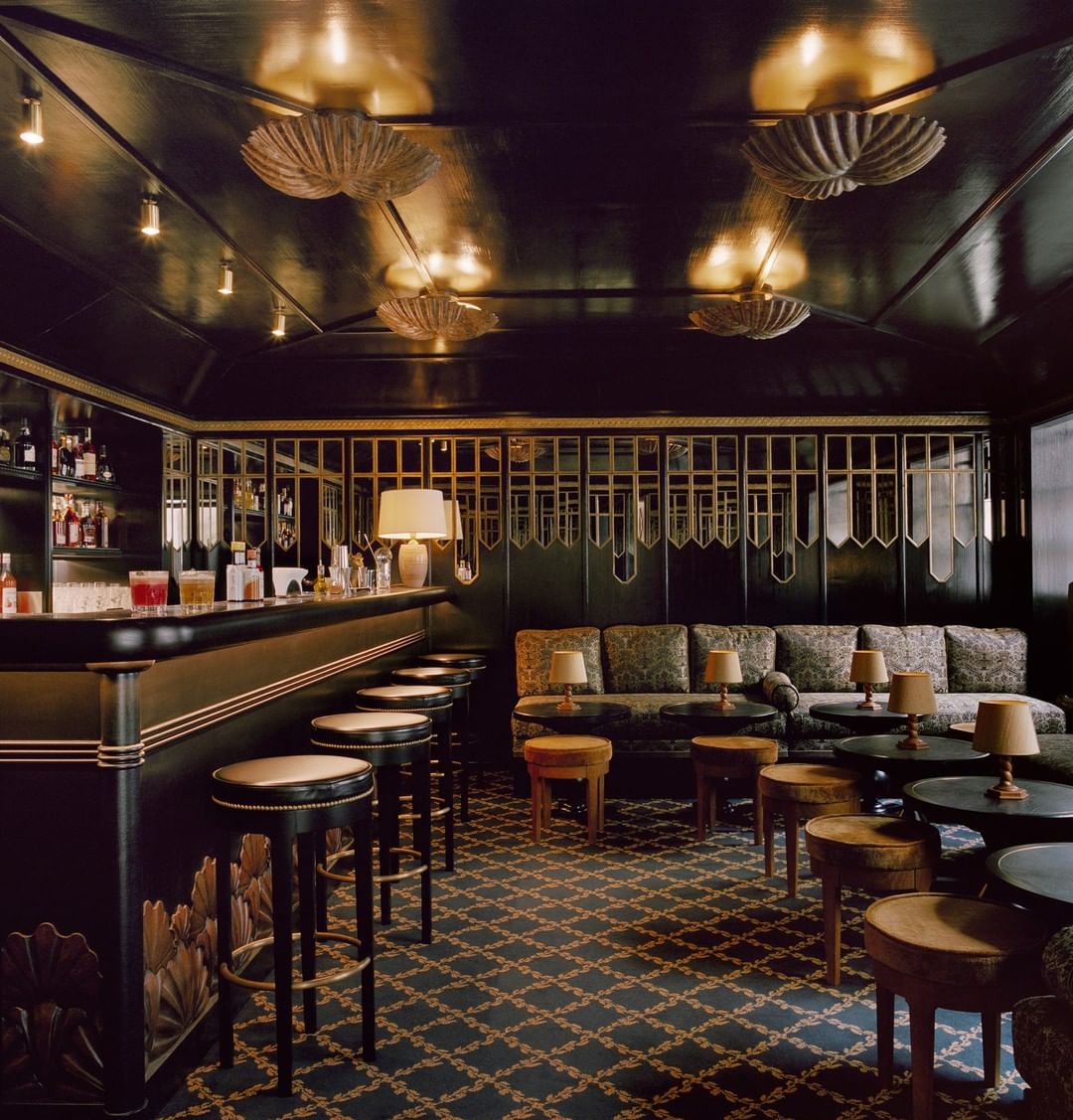 Clubby black + gold bar La Coquille d'Or at Chateau Voltaire in Paris with scallop shell motif lights, hand-crafted wooden table lamps and brass-studded bar stools