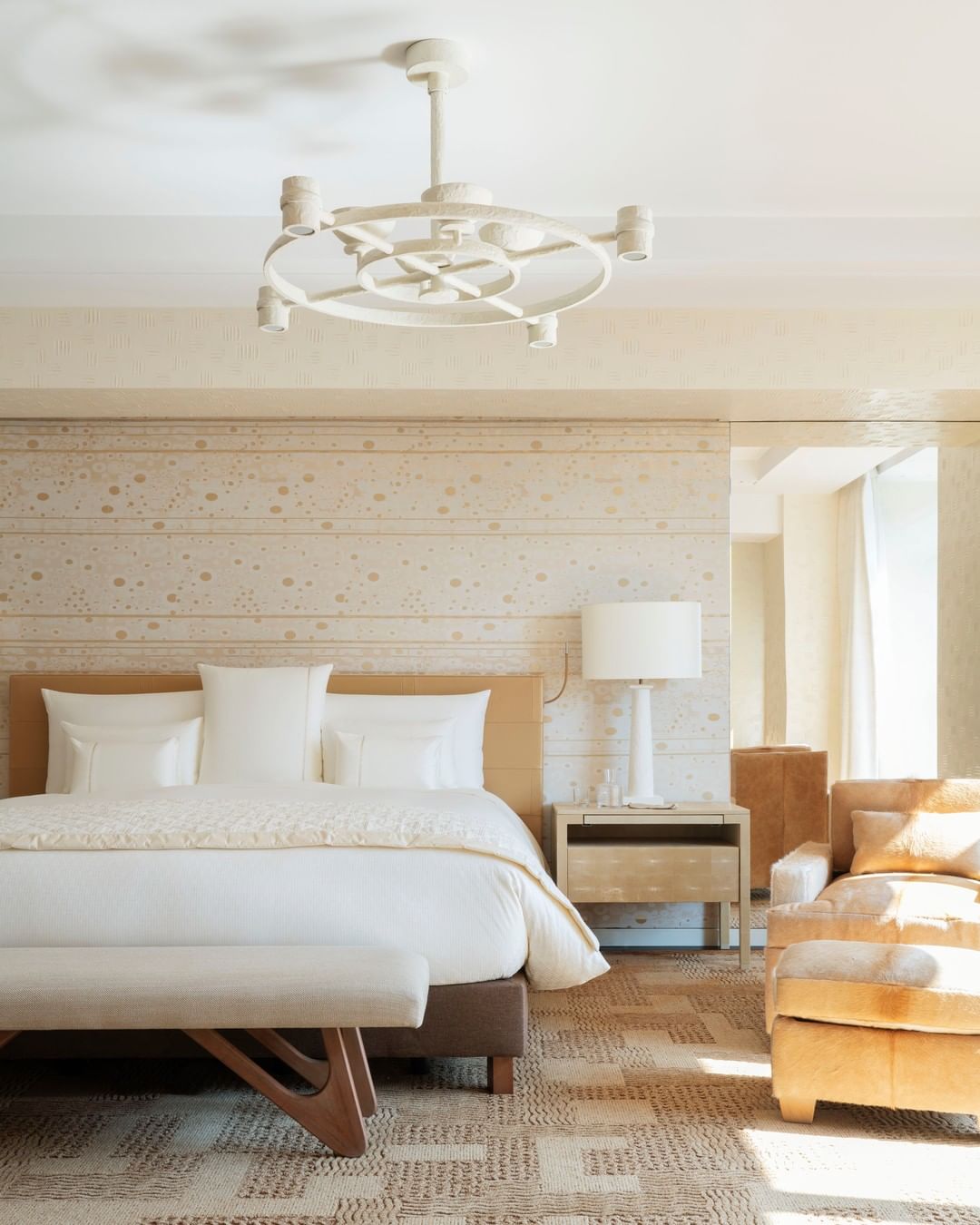 A cream and beige suite at Cheval Blanc Paris featuring mid-century modern furniture and a unique matte white chandelier