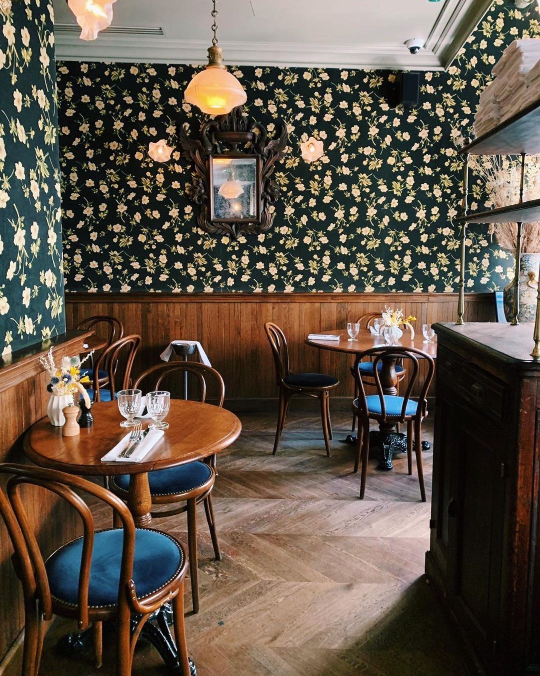 A deep teal wallpaper covered in cream wildflower motifs is juxtaposed by wood-paneled wainscoting at the bistro style bar at Hotel Providence in Paris