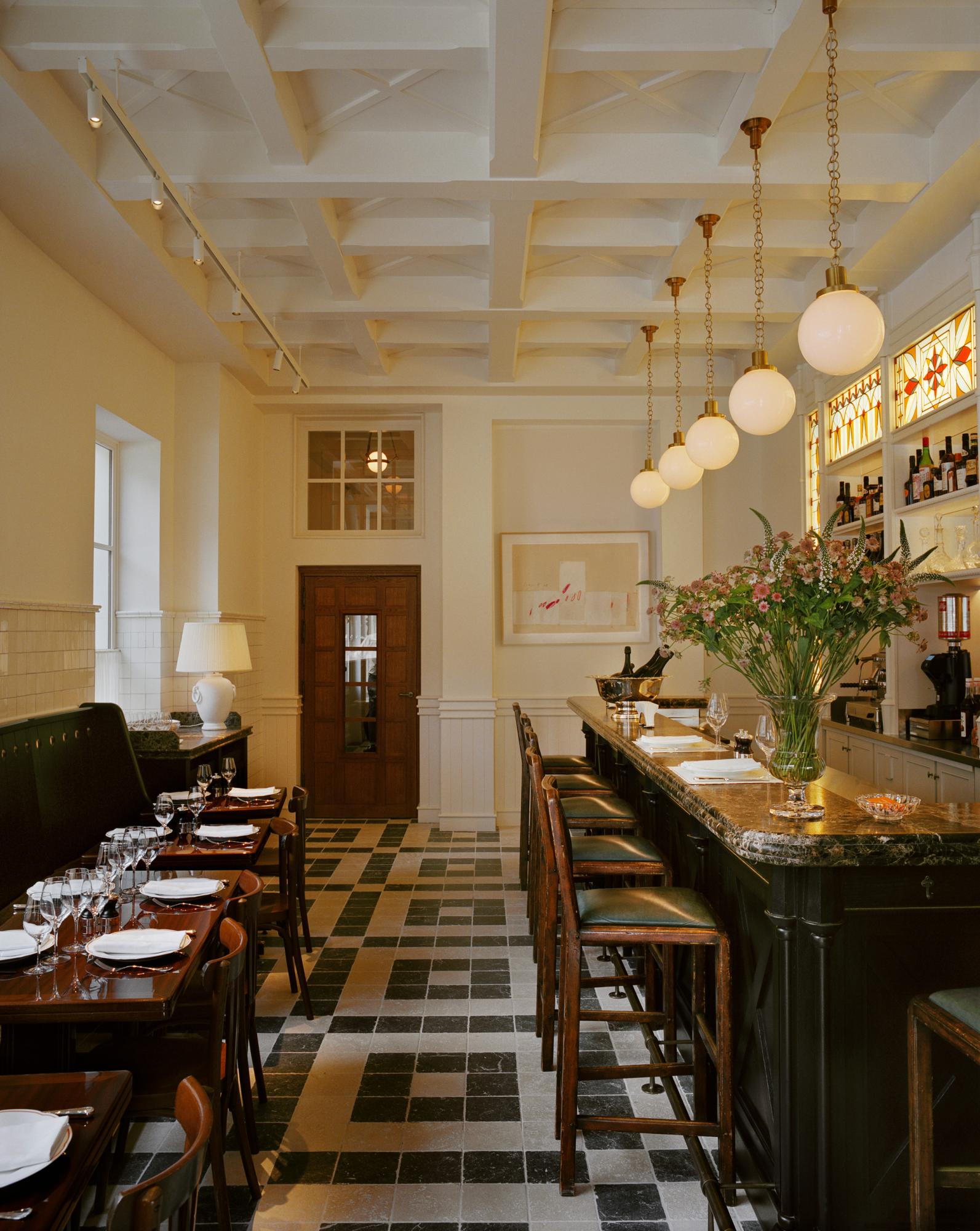 The cozy interiors of Brasserie Emil at Chateau Voltaire with green-leather bar stools, classic banquette seating along the walls and an Art Deco inspired floor made up of black and white stone