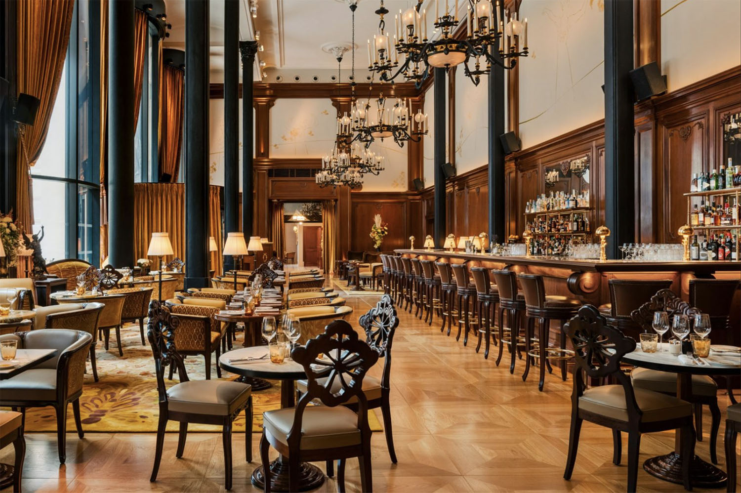 The Belle Epoque inspired interiors of Madame Rêve Cafe with double-height ceilings, wood-paneled walls, leather-cushioned chairs with hand-carved backs, ornate chandeliers and marble top tables