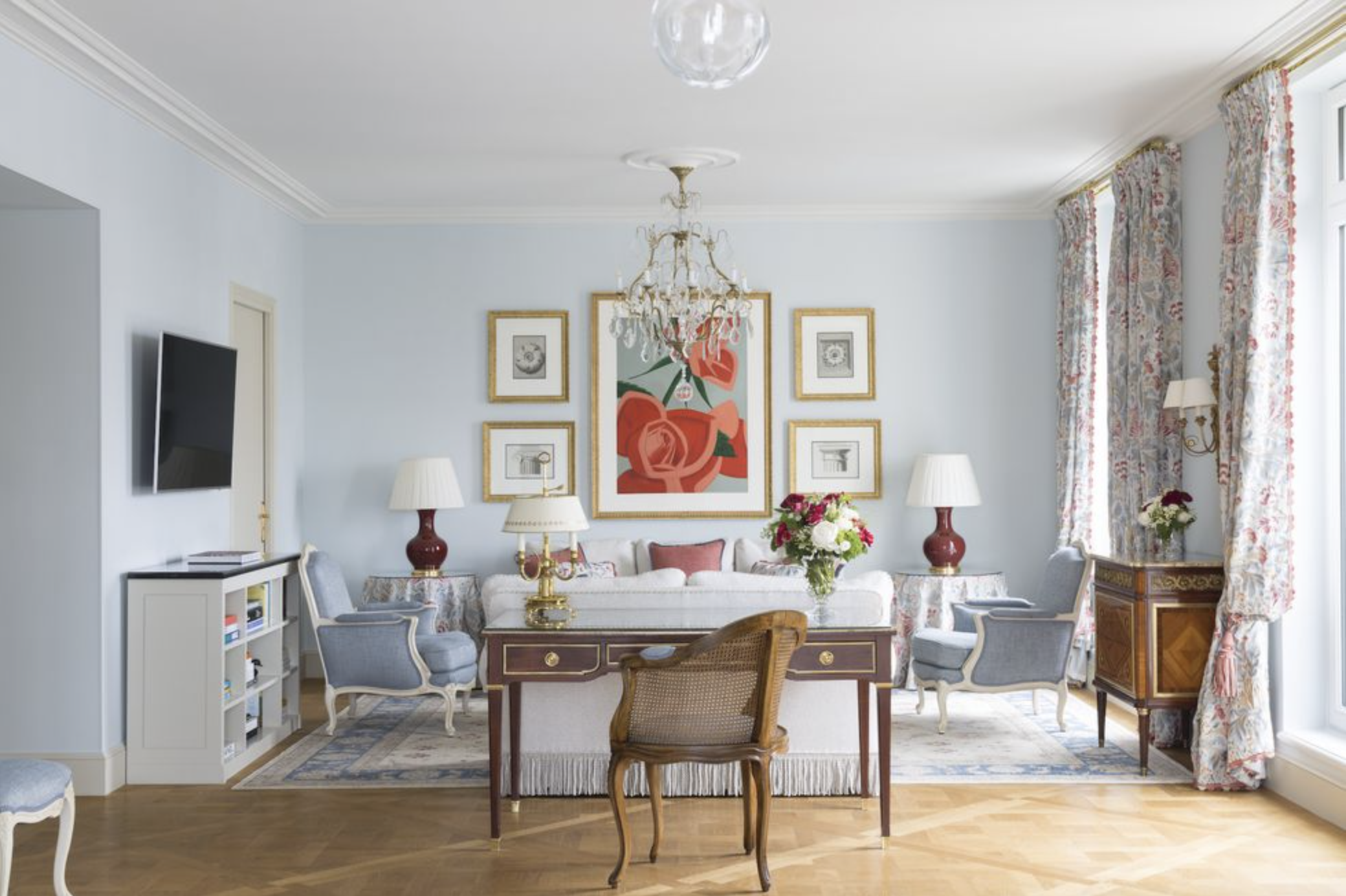 A chic blue guest suite at Le Bristol Paris with an antique wooden writing desk and abstract coral floral art on the gallery wall
