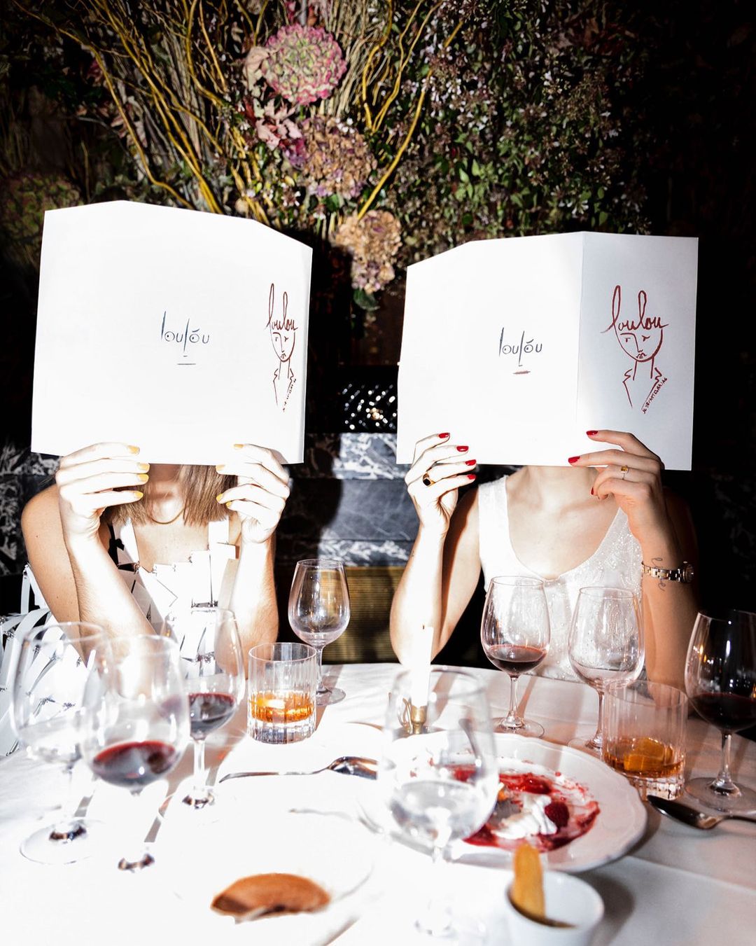 High flash photography at Loulou with two girls holding up the famous menus over their faces