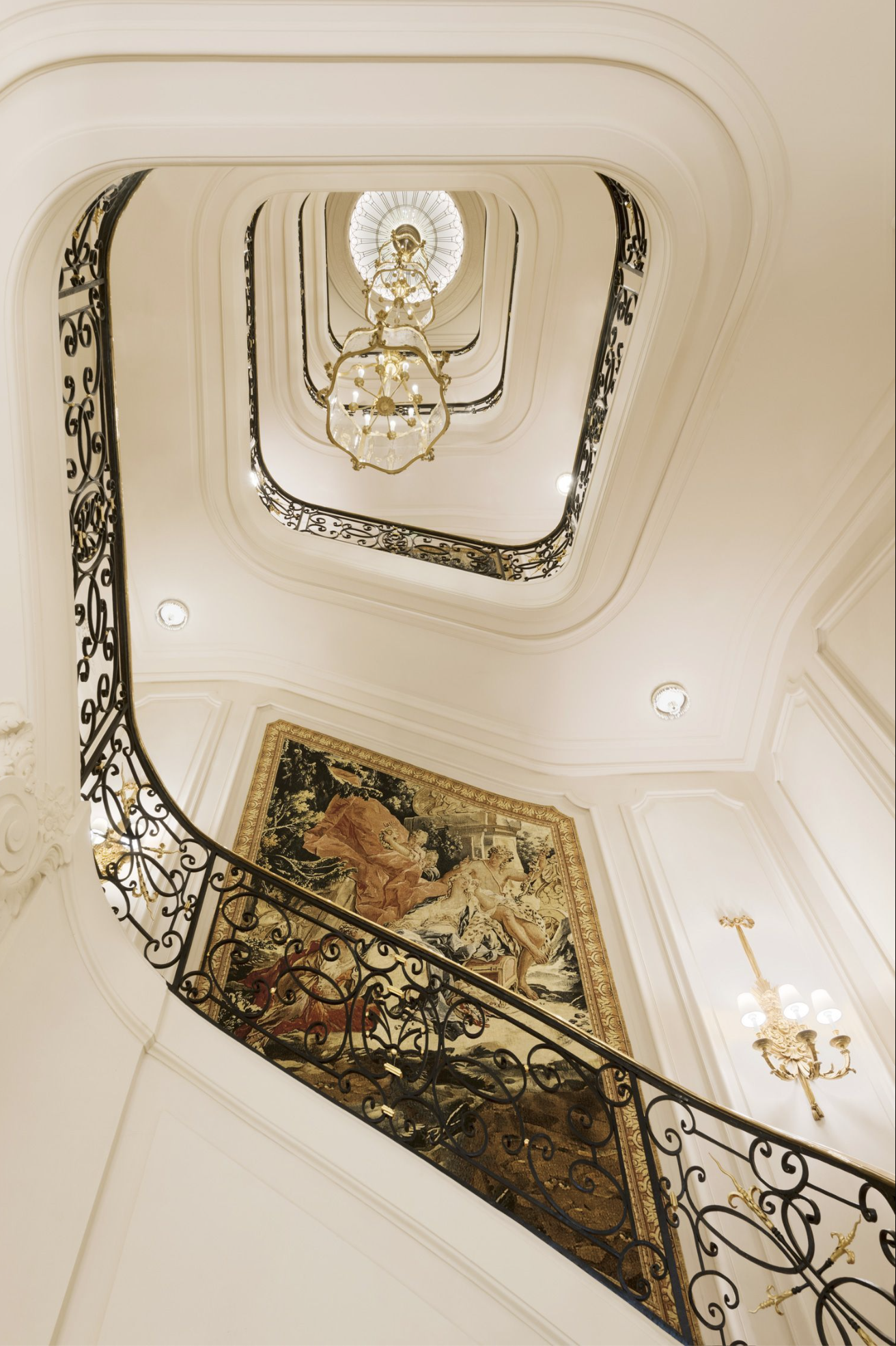 The grand spiral staircase at Ritz Paris featuring an antique tapestry